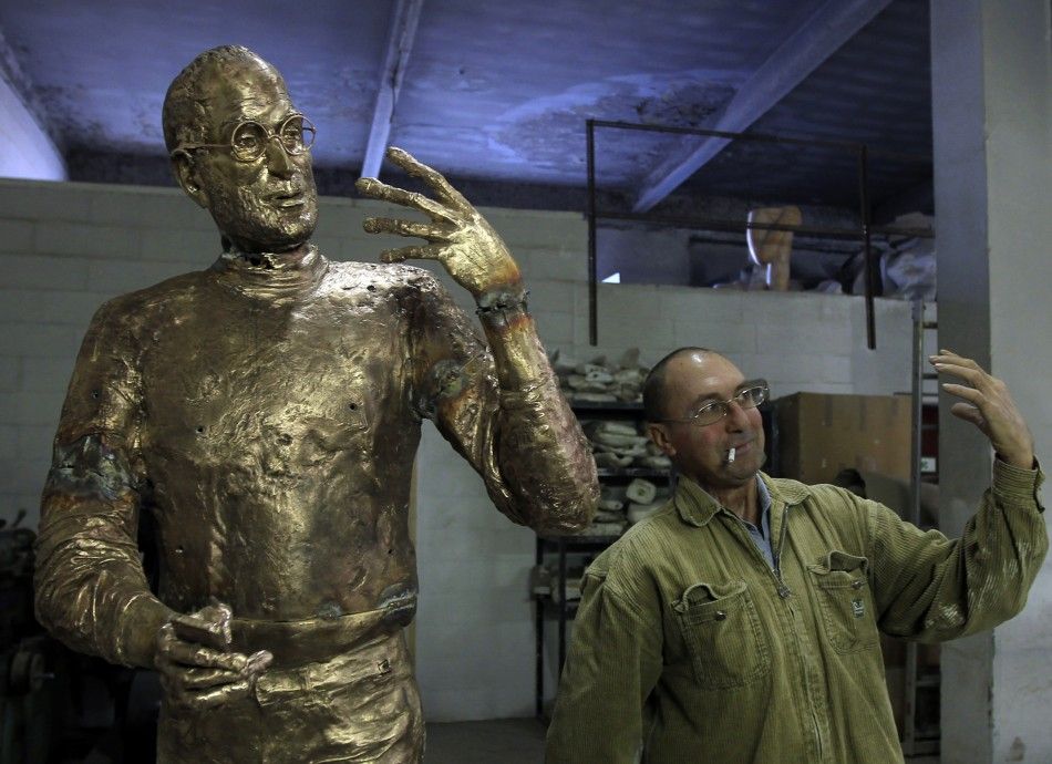 Assistant to Hungarian sculptor Erno Toth mimics the pose of the sculptors latest work, a bronze statue of late Apple co-founder Steve Jobs, in Budapest