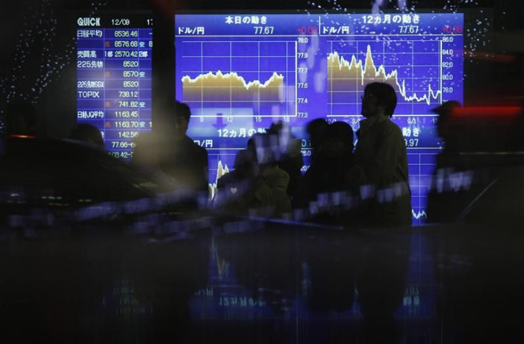 Passersby walk in front of an electric board displaying movements of the Japanese yen&#039;s exchange rate against the U.S. dollar outside a brokerage in Tokyo