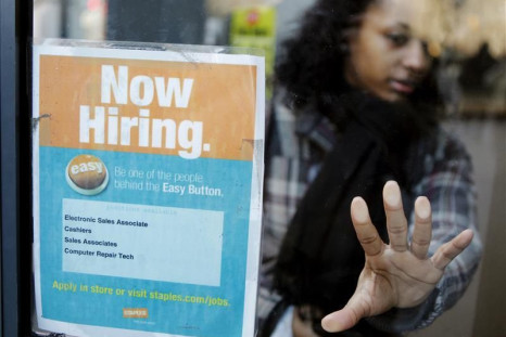 A woman opens a glass door with a &quot;Now Hiring&quot; sign on it as she enters a Staples store in New York