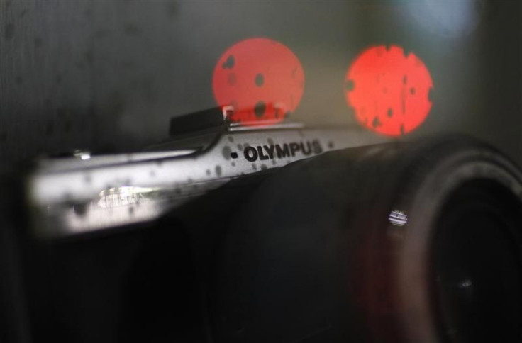 Olympus Corp's digital camera is seen through a show window which bears rain drops and reflects lights from traffic at an electronic shop in Tokyo