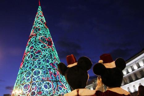 Two people dressed as Mickey Mouse stand next to Christmas tree made out of lights as they wait to perform for children at Puerta del Sol square