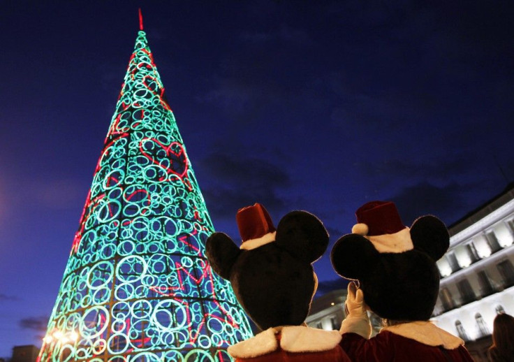 Two people dressed as Mickey Mouse stand next to Christmas tree made out of lights as they wait to perform for children at Puerta del Sol square
