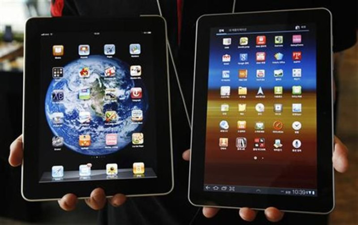 An employee of South Korean mobile carrier KT holds a Samsung Electronics&#039; Galaxy Tab 10.1 tablet and Apple Inc&#039;s iPad tablet as he poses in Seoul