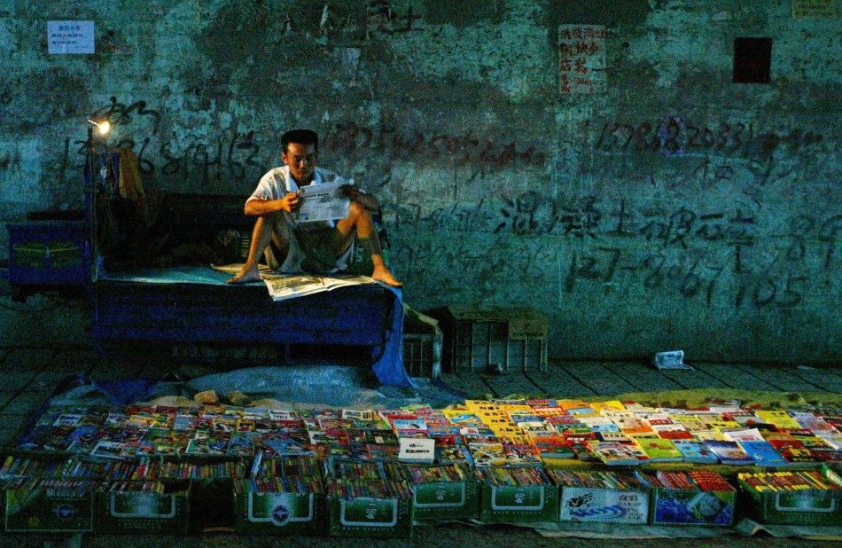 Chinese vendor reads a newspaper while selling books in Jinan.