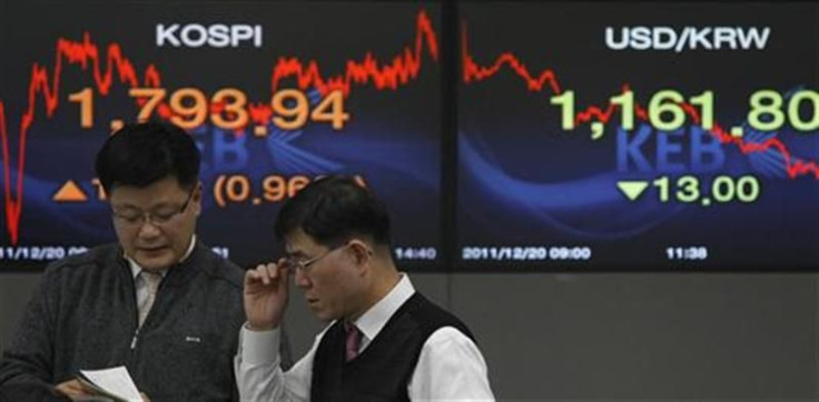 Currency dealers talk in front of screens showing the stock price index and the exchange rate between the South Korean won and the dollar at a bank in Seoul