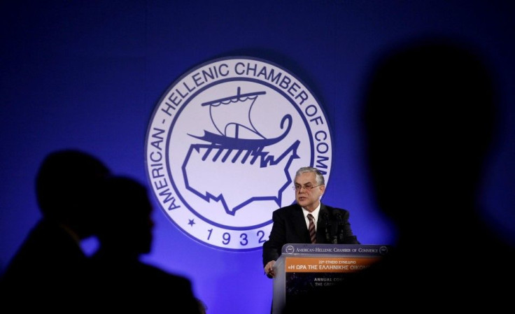Greece's Prime Minister Lucas Papademos addresses the audience as officers of his personal security are silhouetted in front of him during an economic conference in Athens December 14, 2011.