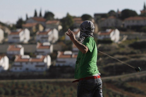 The West Bank Jewish settlement of Halamish is seen in the background as a Palestinian demonstrator uses a sling to throw a stone towards Israeli soldiers during clashes near Ramallah