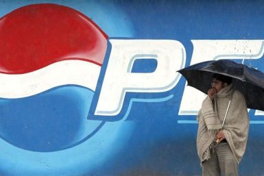 A man stands next to a Pepsi advertisement while using an umbrella in the rain, in Rawalpindi