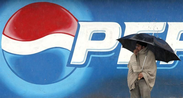 A man stands next to a Pepsi advertisement while using an umbrella in the rain, in Rawalpindi