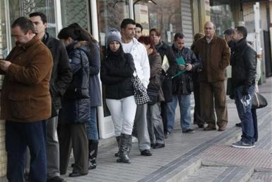People wait in line for the opening of a government employment office in Madrid