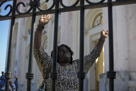 A woman raises her arms while praying outside a destroyed cathedral in downtown Port-au-Prince