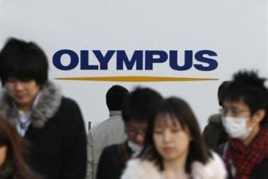 People walk past a signboard of Olympus Corp outside its showroom in Tokyo January 12, 2012.