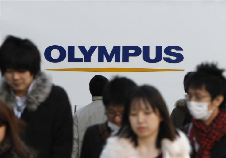 People walk past a signboard of Olympus Corp outside its showroom in Tokyo