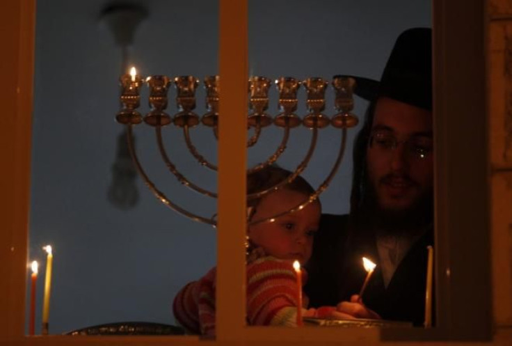 208881-an-ultra-orthodox-jewish-man-holds-a-child-as-he-lights-a-candle-for-h