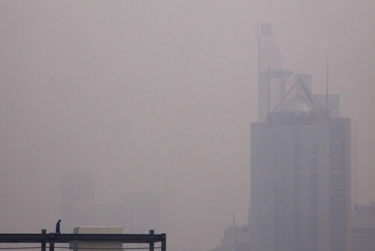 A worker stands atop a building under construction on a hazy day in Beijing