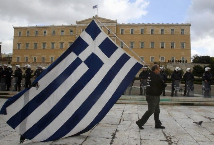 A striker parades with a huge Greek flag in front of riot police guarding the parliament in central Athens