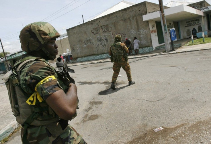 Soldiers patrol a street in the Tivoli Gardens neighborhood of Kingston with foreign journalists escorted into the area