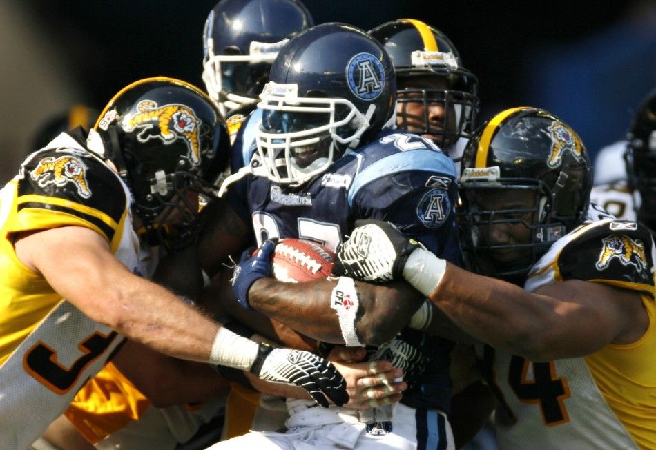 Toronto Argonauts running back Ricky Williams C is grabbed by Hamilton Tiger-Cats Agustin Barrenechea L and Devonte Peterson R during his first regular season CFL football game in Toronto