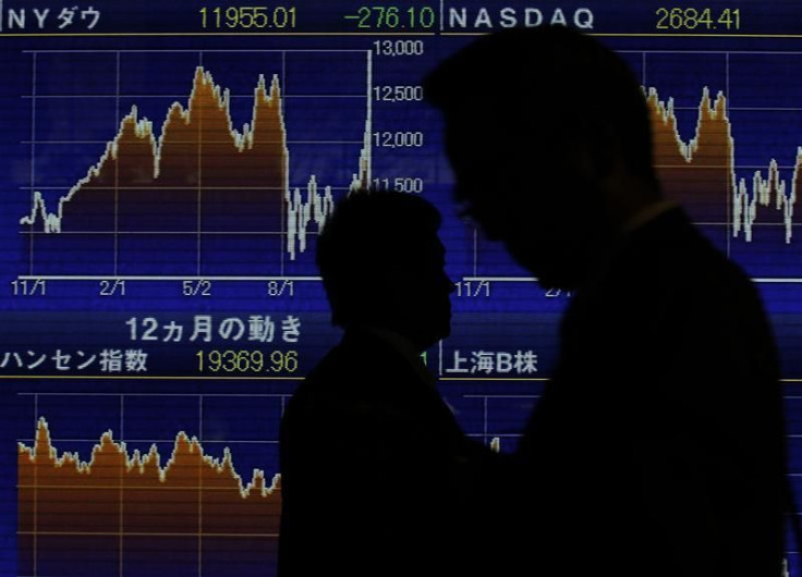 People walk past an electronic board displaying graphs of various market indices from around the world outside a brokerage in Tokyo