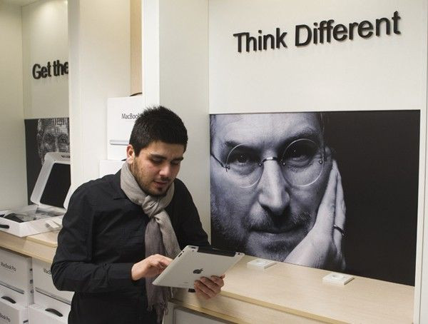 Man checks Apple iPad as he stands next to portrait of late Apple co-founder Jobs at shop in Payetakht computer centre in northern Tehran