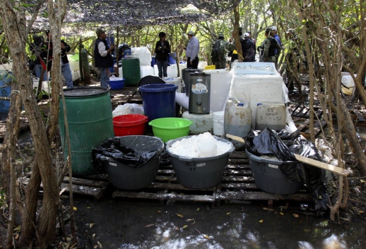 Soldiers and investigators stand near drums and ingredients to make crystal methamphetamines at a clandestine drug processing laboratory