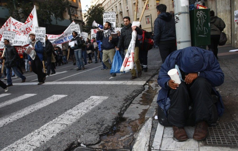 Greece A homeless man begs for money as a demonstration against economic austerity measures passes him by in Athens Sunday.