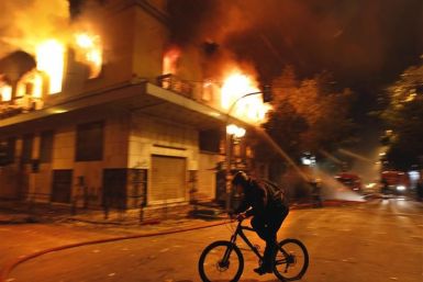 A cyclist rides past a burning building during violent protests in central Athens