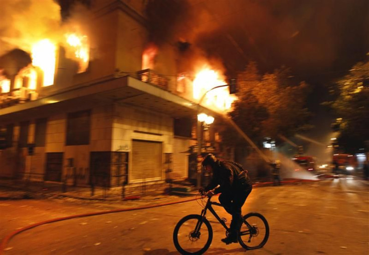 A cyclist rides past a burning building during violent protests in central Athens